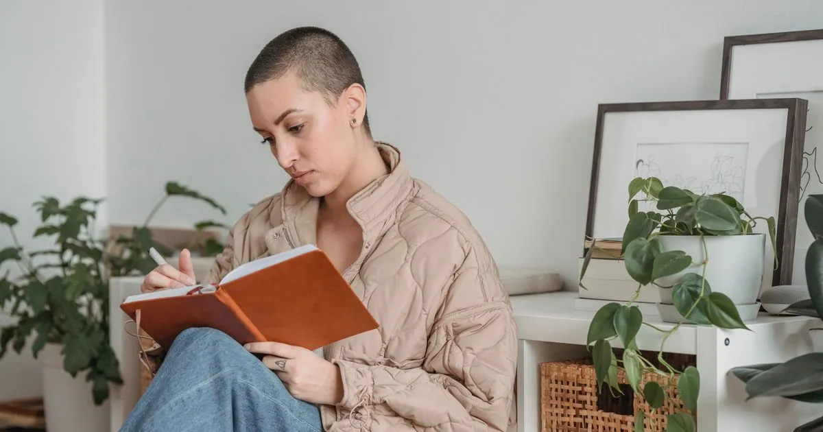 Mulher adulta escrevendo um exercício de autoconhecimento à mão em um caderno, em casa, sob luz natural