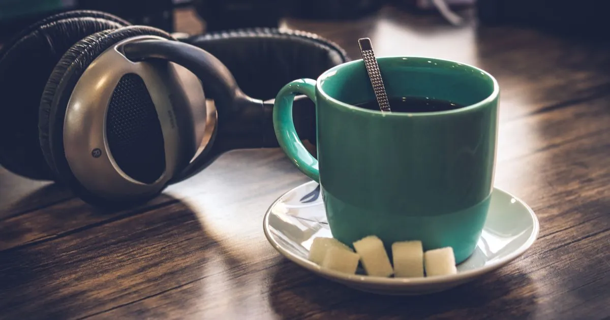 Fone de ouvido sobre a mesa de madeira, ao lado de uma xícara de café, na luz quente de um início de noite em casa.