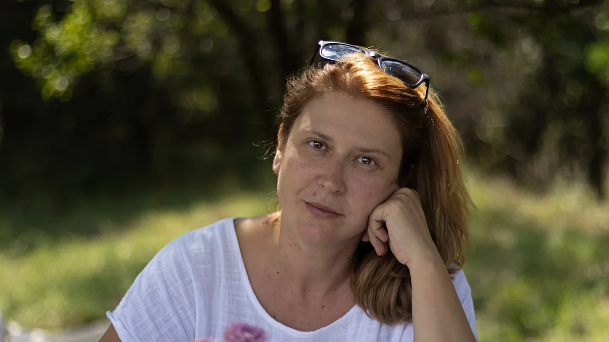 Mulher por volta dos 45 anos ao ar livre, na luz natural do fim da tarde, com a mão apoiada no rosto e um olhar calmo e atento