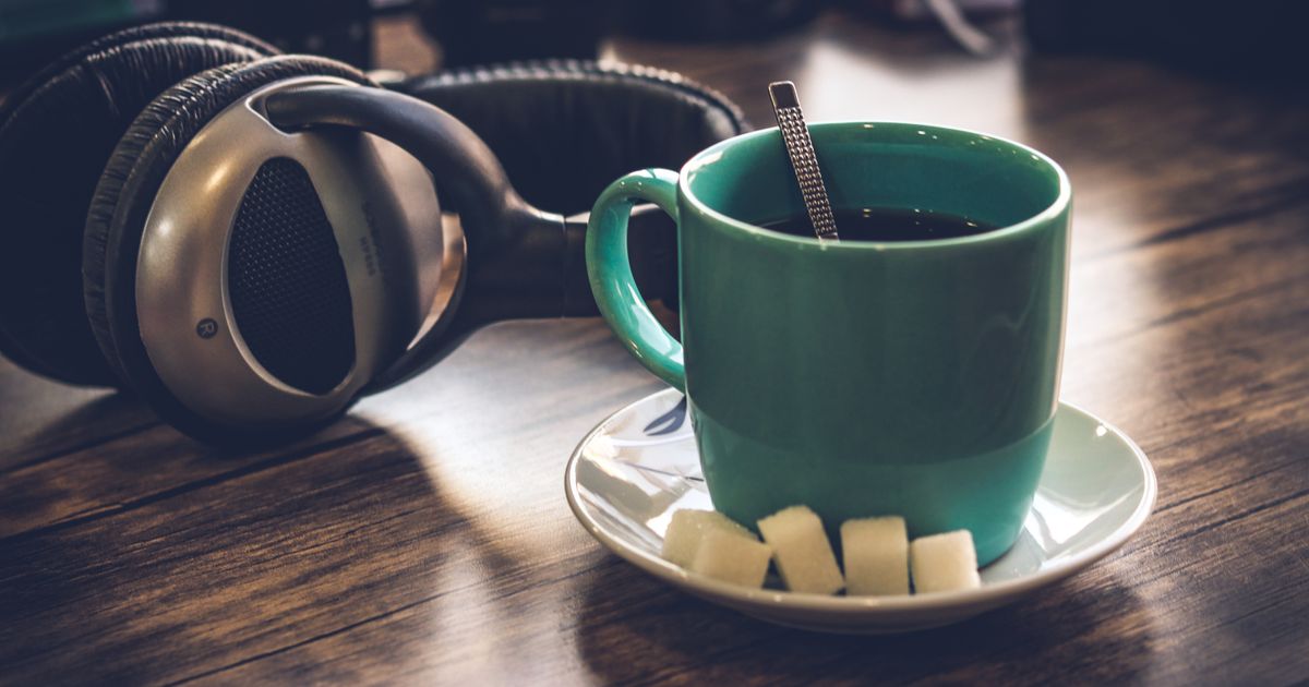 Fone de ouvido sobre a mesa de madeira, ao lado de uma xícara de café, na luz quente de um início de noite em casa.