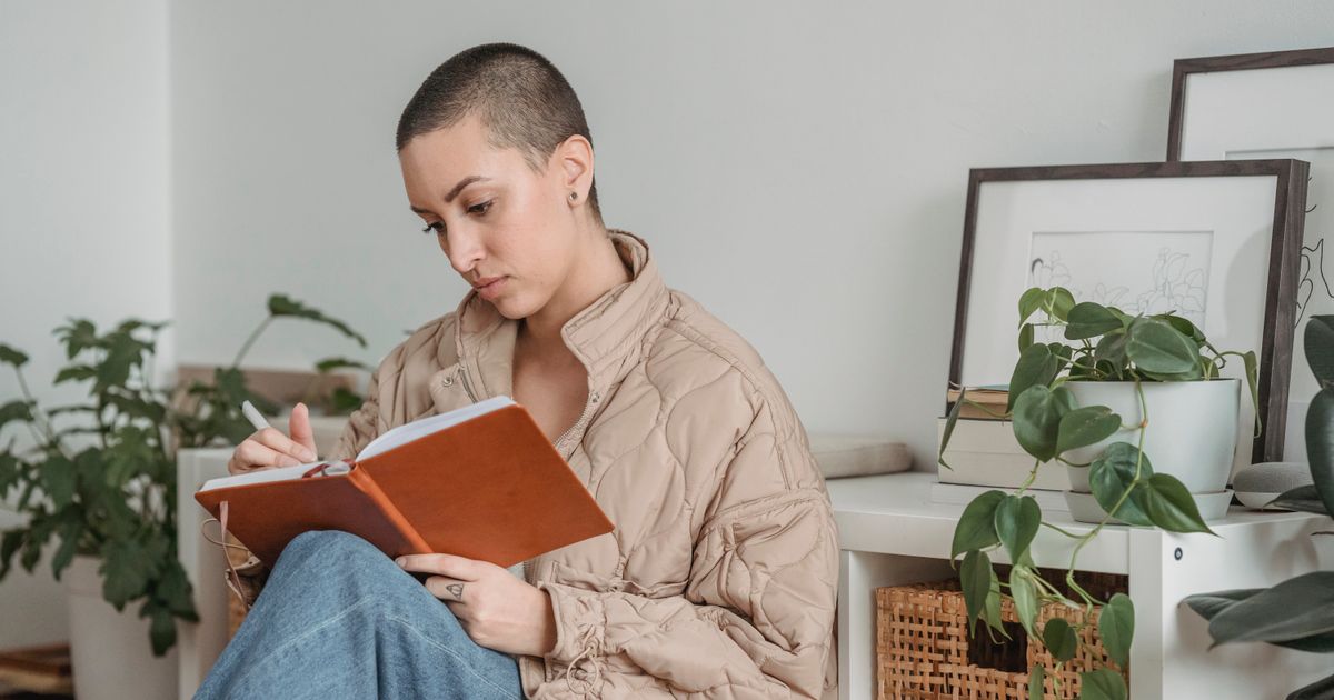 Mulher adulta escrevendo um exercício de autoconhecimento à mão em um caderno, em casa, sob luz natural