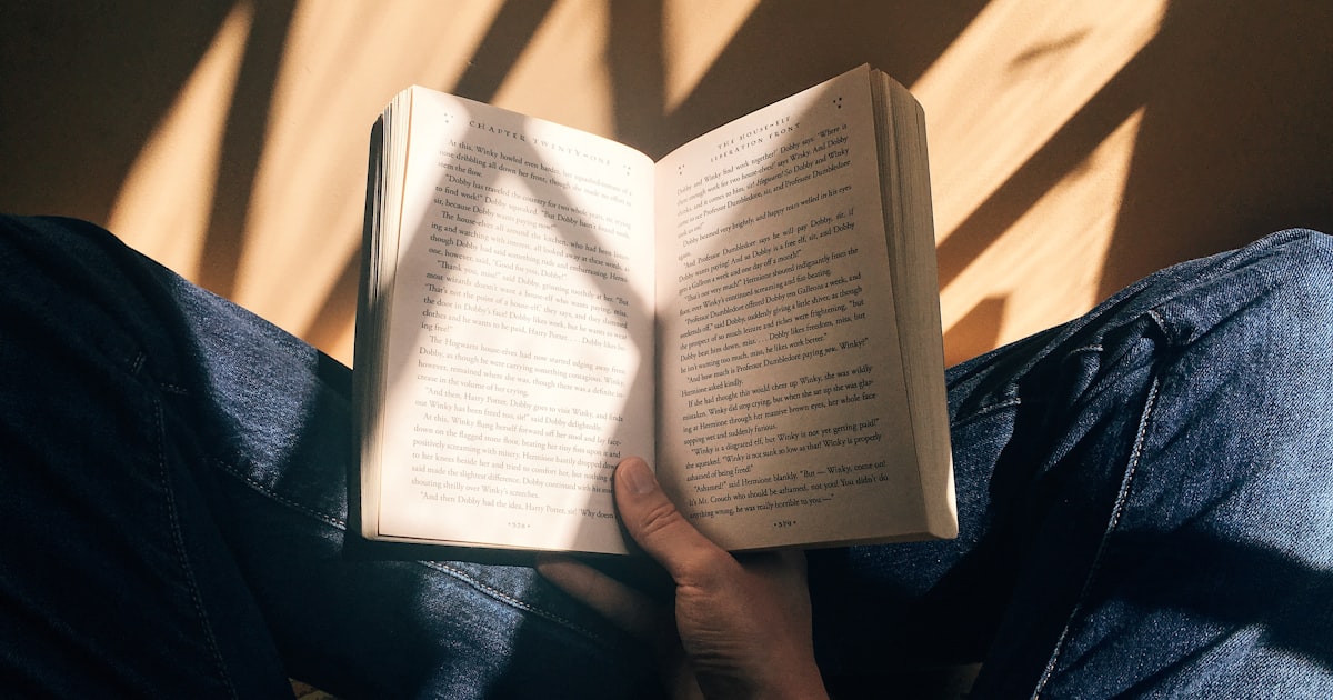 Pessoa lendo um livro no colo sob luz natural quente entrando pela janela