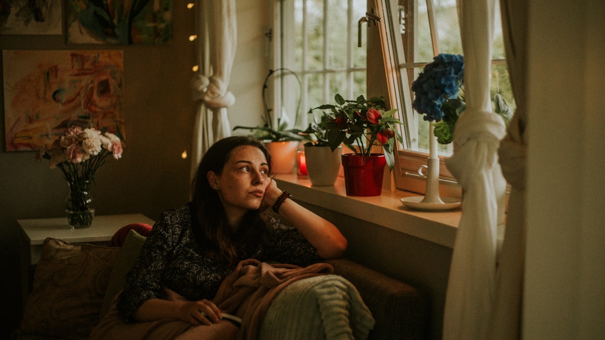 Mulher em um canto tranquilo de casa, perto da janela, em uma pausa de introspecção sob luz suave e acolhedora