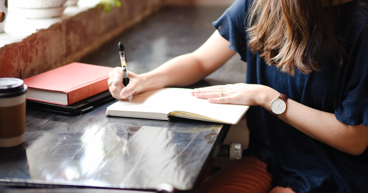 Mulher escrevendo num caderno perto da janela, sob luz natural quente