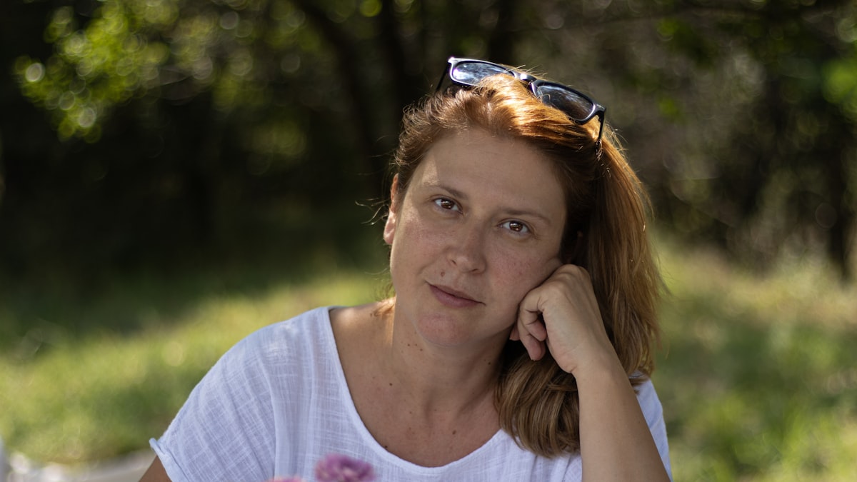 Mulher por volta dos 45 anos ao ar livre, na luz natural do fim da tarde, com a mão apoiada no rosto e um olhar calmo e atento