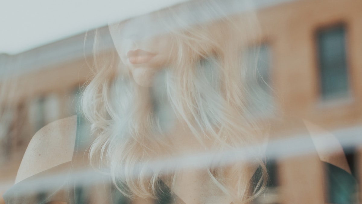 Reflexo suave do rosto de uma mulher no vidro de uma janela, em luz quente, sugerindo o olhar para dentro e a relação consigo mesma.