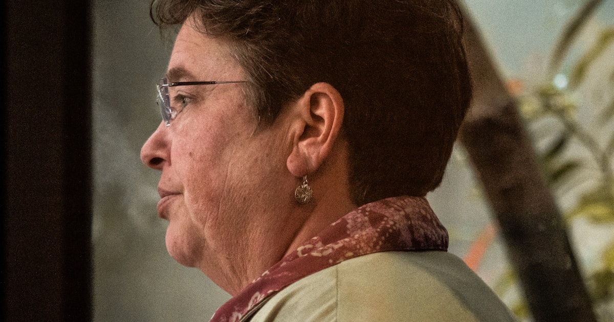 Mulher madura de óculos, em perfil, olhando para longe sob luz natural quente, num momento de escuta e introspecção